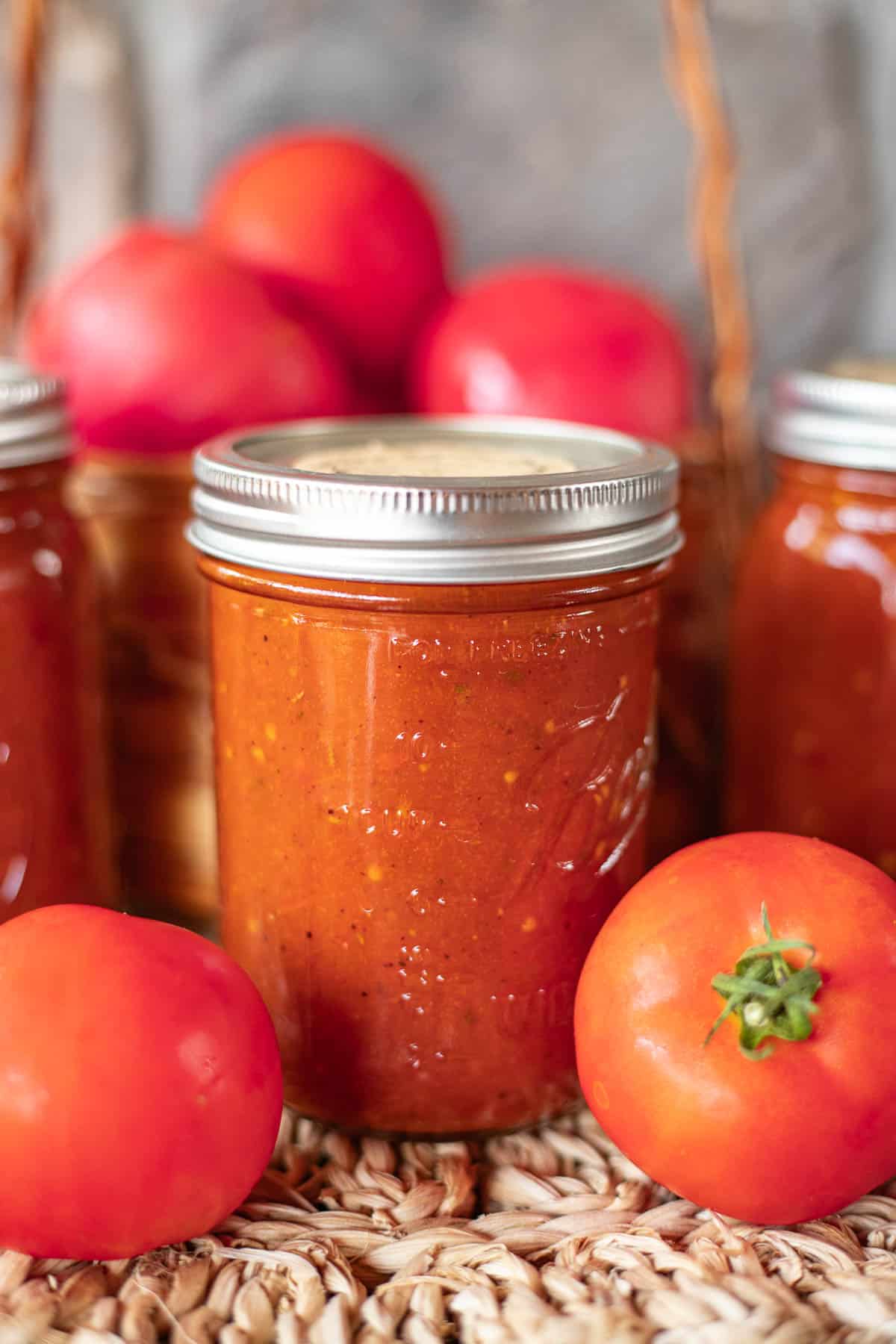 roasted tomato pasta sauce in jars with tomatoes around it.