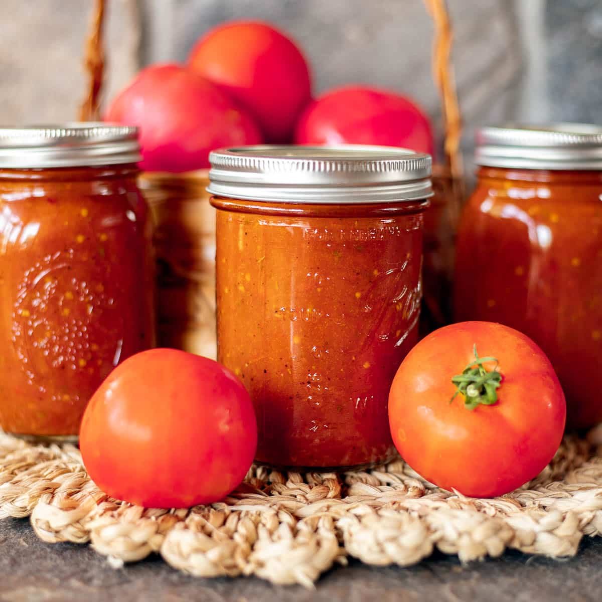 roasted tomato pasta sauce in jars with tomatoes around it.