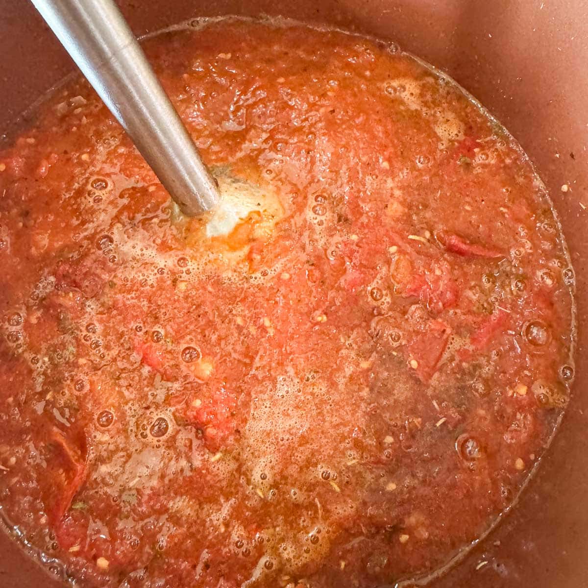 using an immersion blender to blend roasted tomato sauce.