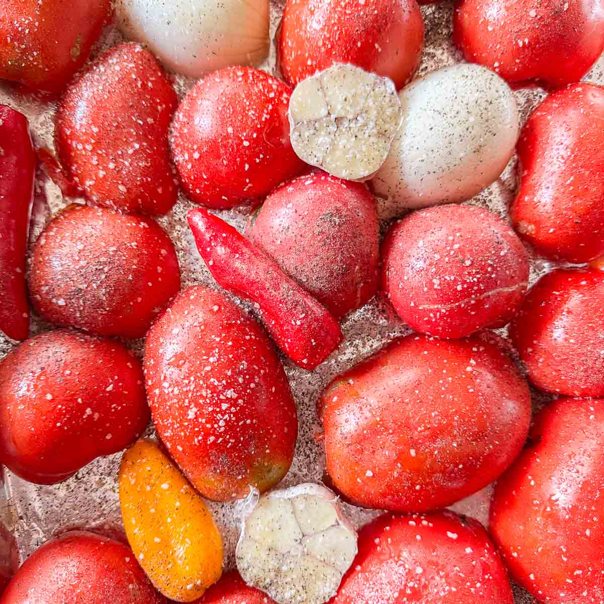seasoned tomatoes, peppers, onion, and garlic on a baking sheet.