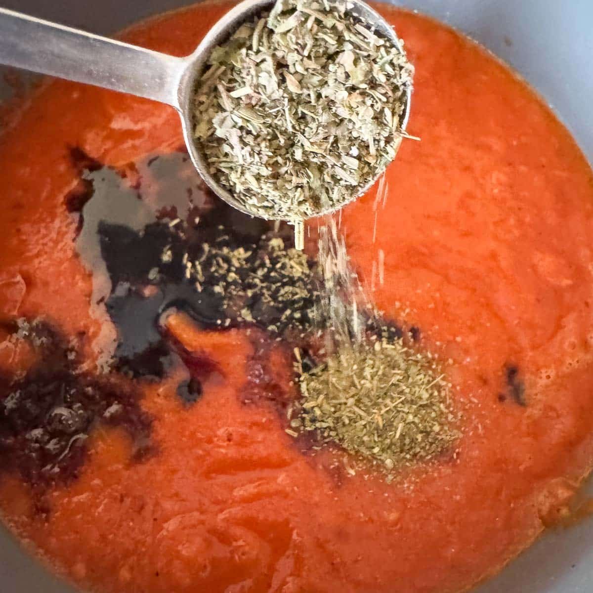 adding herbs to roasted tomato pasta sauce in a pot.