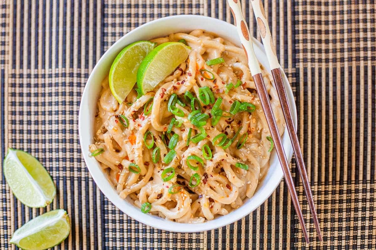 spicy peanut noodles in bowl beside lime wedges.