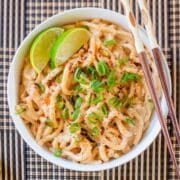 spicy peanut noodles in bowl with lime wedges.