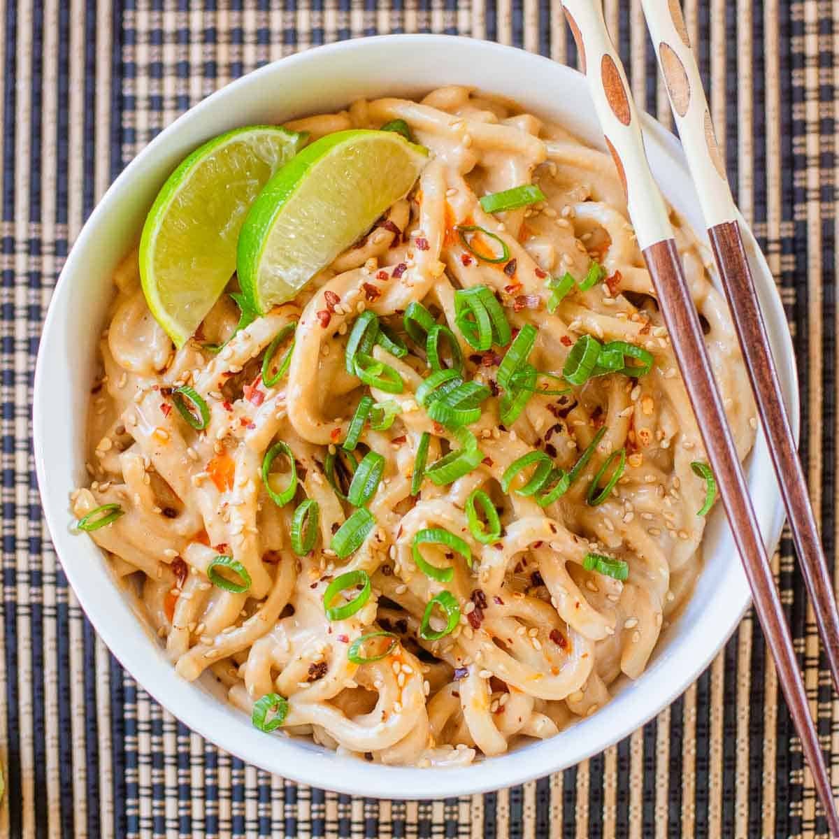spicy peanut noodles in bowl with lime wedges.