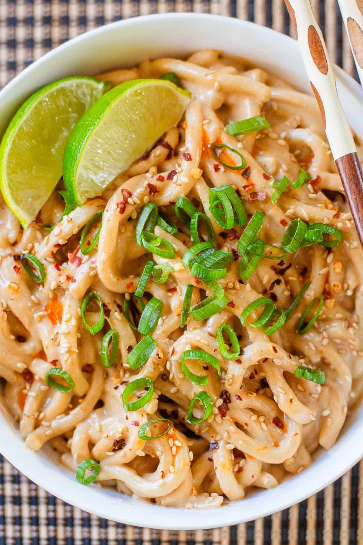 spicy peanut noodles in bowl with lime wedges.