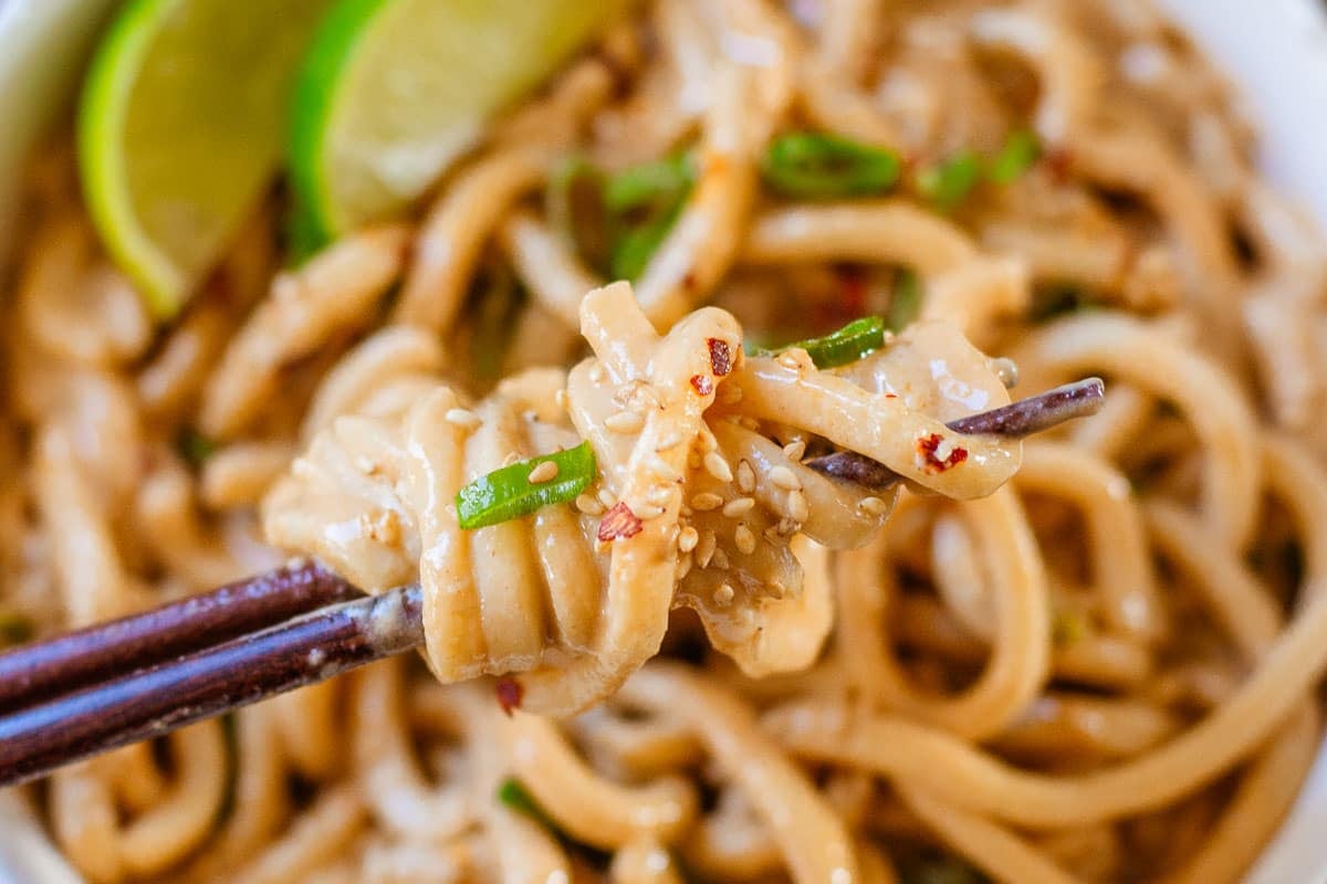 spicy peanut noodles wrapped around chopsticks held above bowl of noodles.