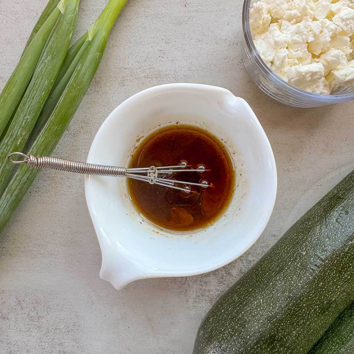 dressing in a white bowl with zucchini, onion, and feta cheese. 
