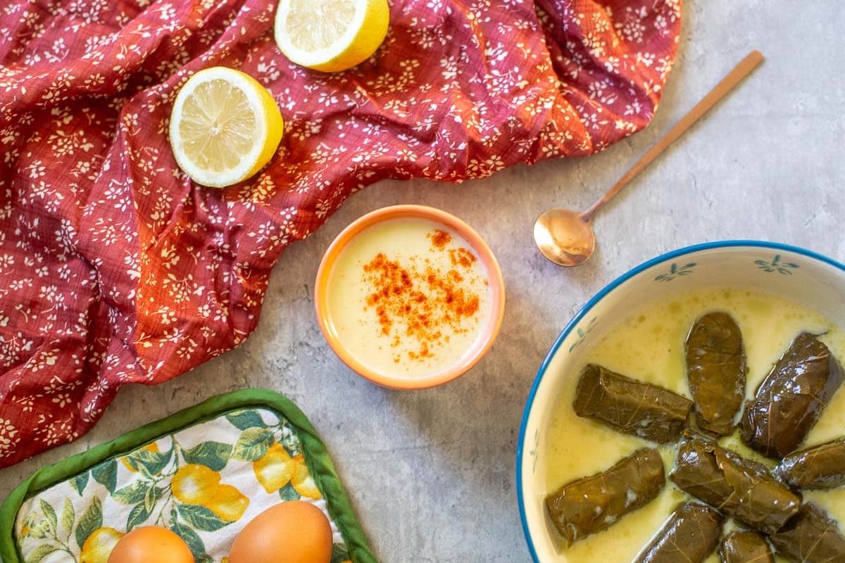 avgolemono sauce in small bowl beside dolmades, lemons, and eggs.