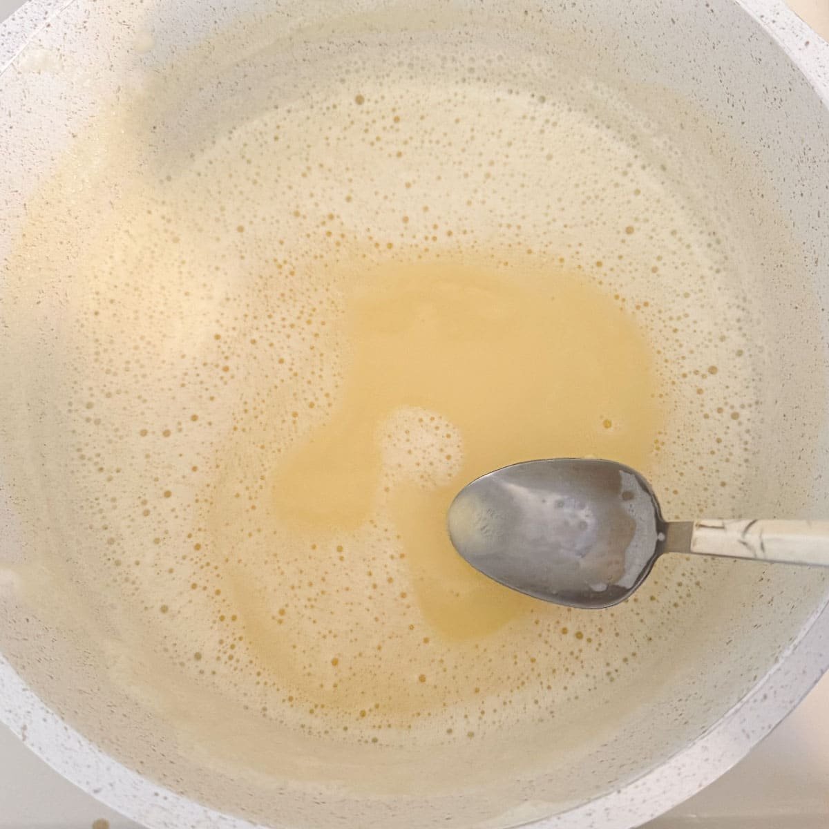 avgolemono in pot with some froth and a spoon.