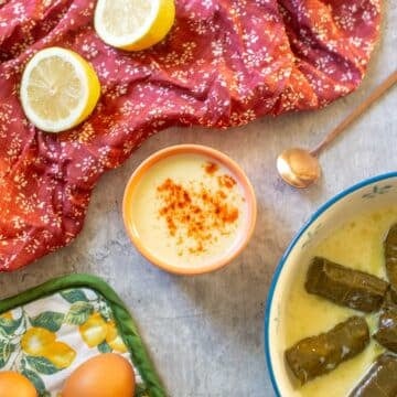 avgolemono sauce in small bowl beside dolmades, lemons, and eggs.
