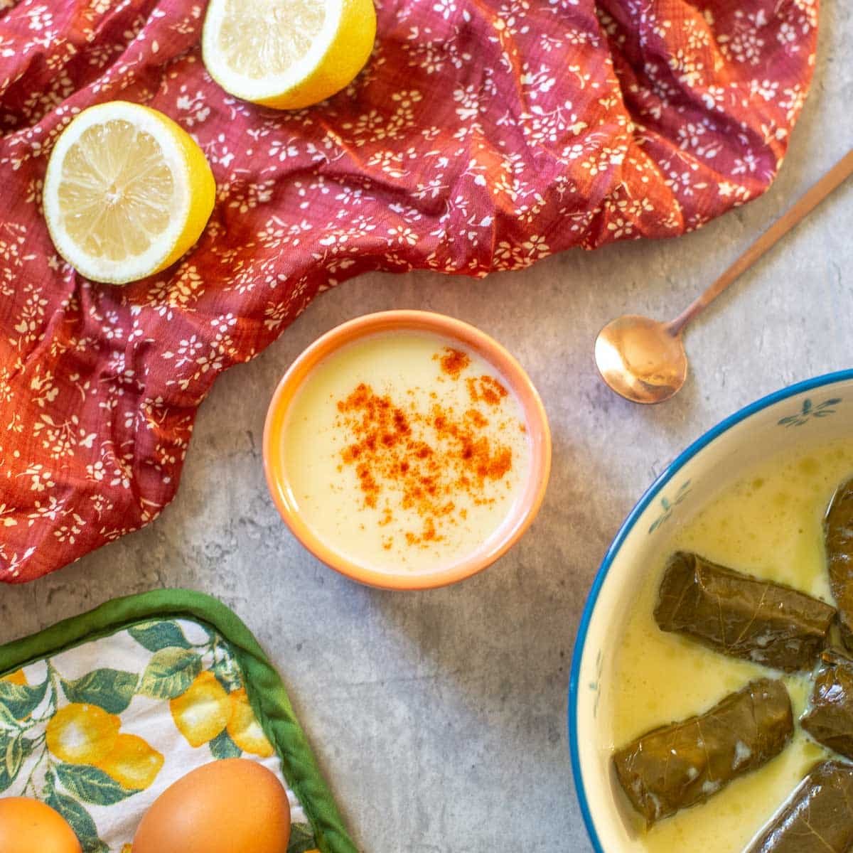 avgolemono sauce in small bowl beside dolmades, lemons, and eggs.