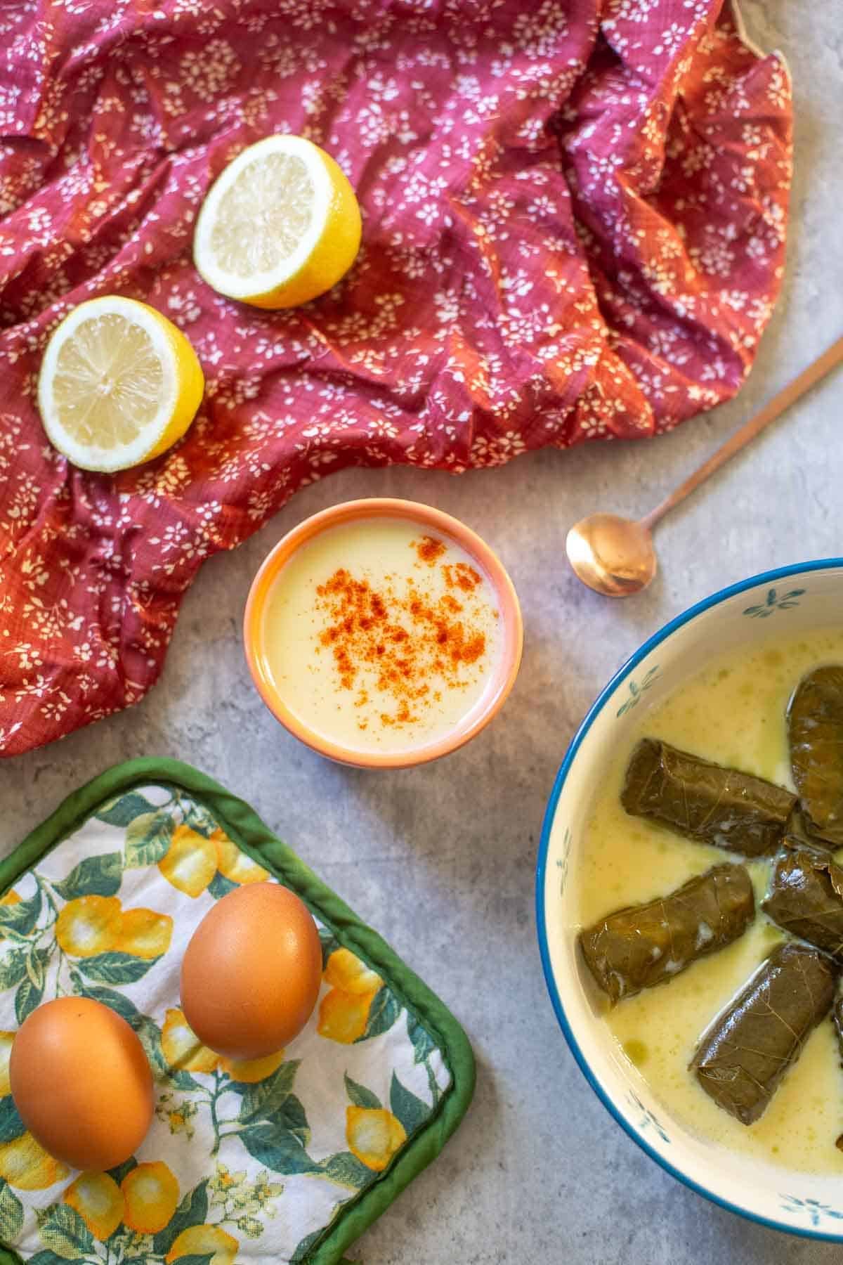 avgolemono sauce in small bowl beside dolmades, lemons, and eggs.