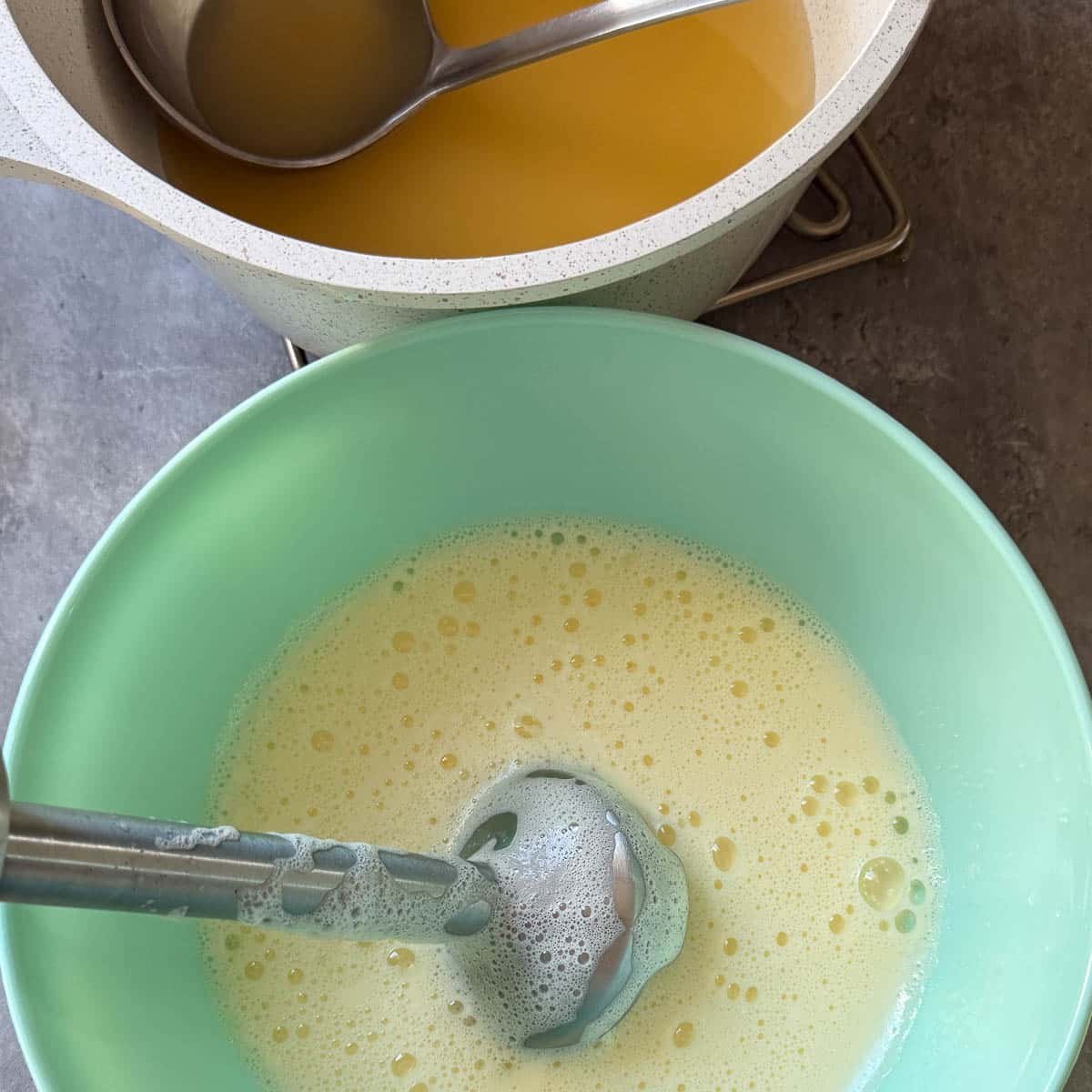 broth in ladle beside bowl of egg-lemon mixture being blended.
