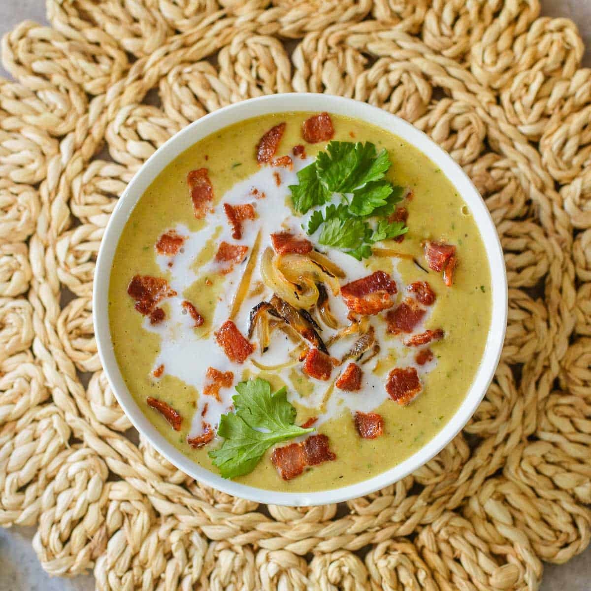 green bacon and lentil soup with lime and cilantro on top in bowl on rattan placemat.