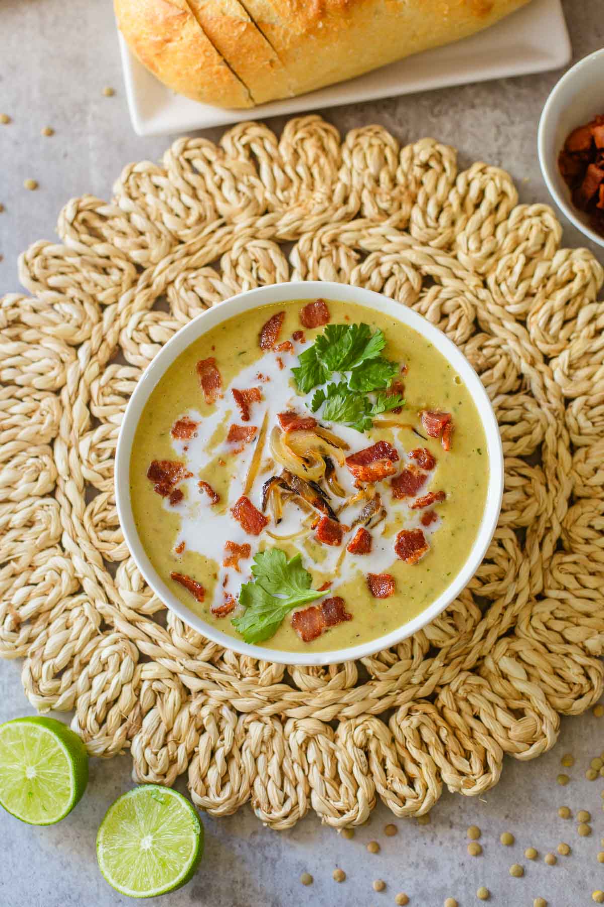 green bacon and lentil soup with lime and cilantro on top on rattan mat with limes, bread, cup of bacon.