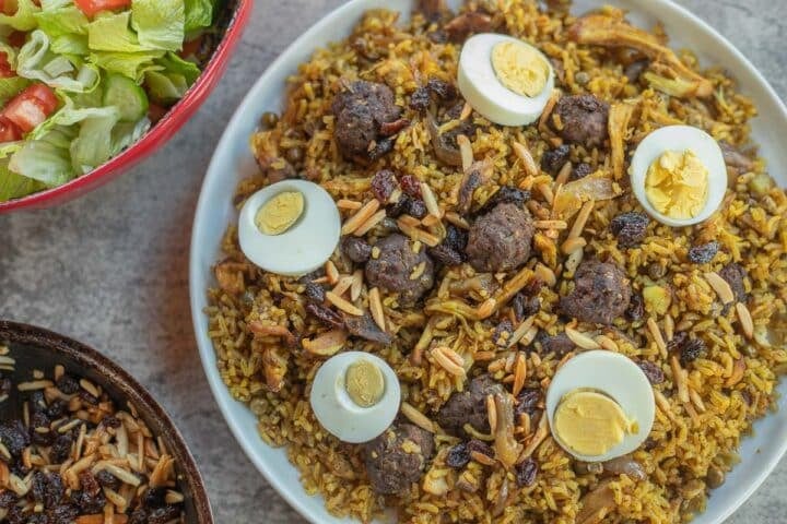 chicken biryani recipe with a salad bowl and some toasted almonds and raisins next to it. 