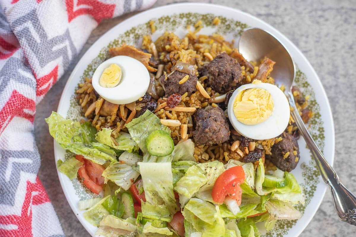 a plate of chicken biryani topped with sliced boiled eggs and a salad.