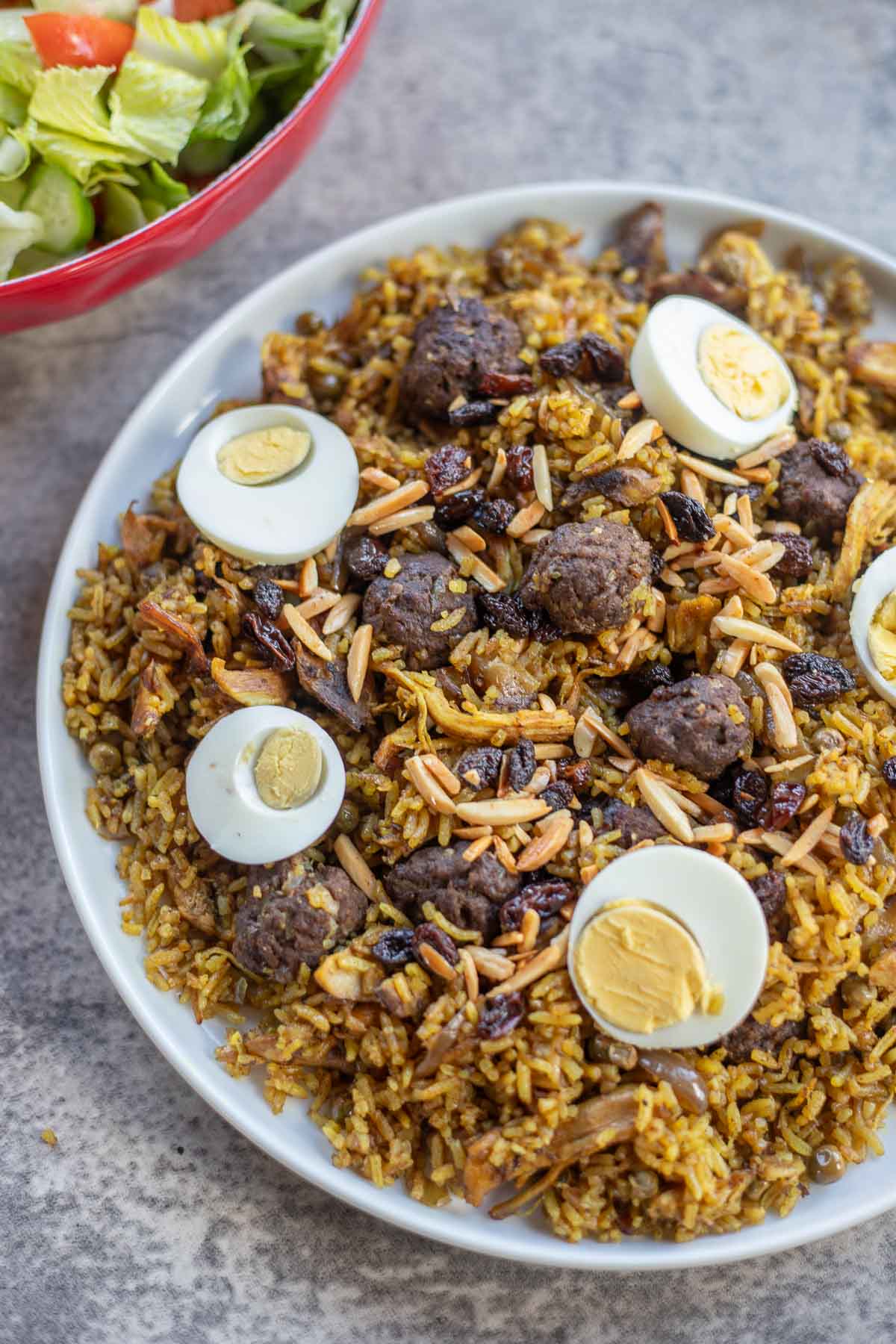 chicken biryani topped with boiled eggs, raisins, and almonds with a side of salad.