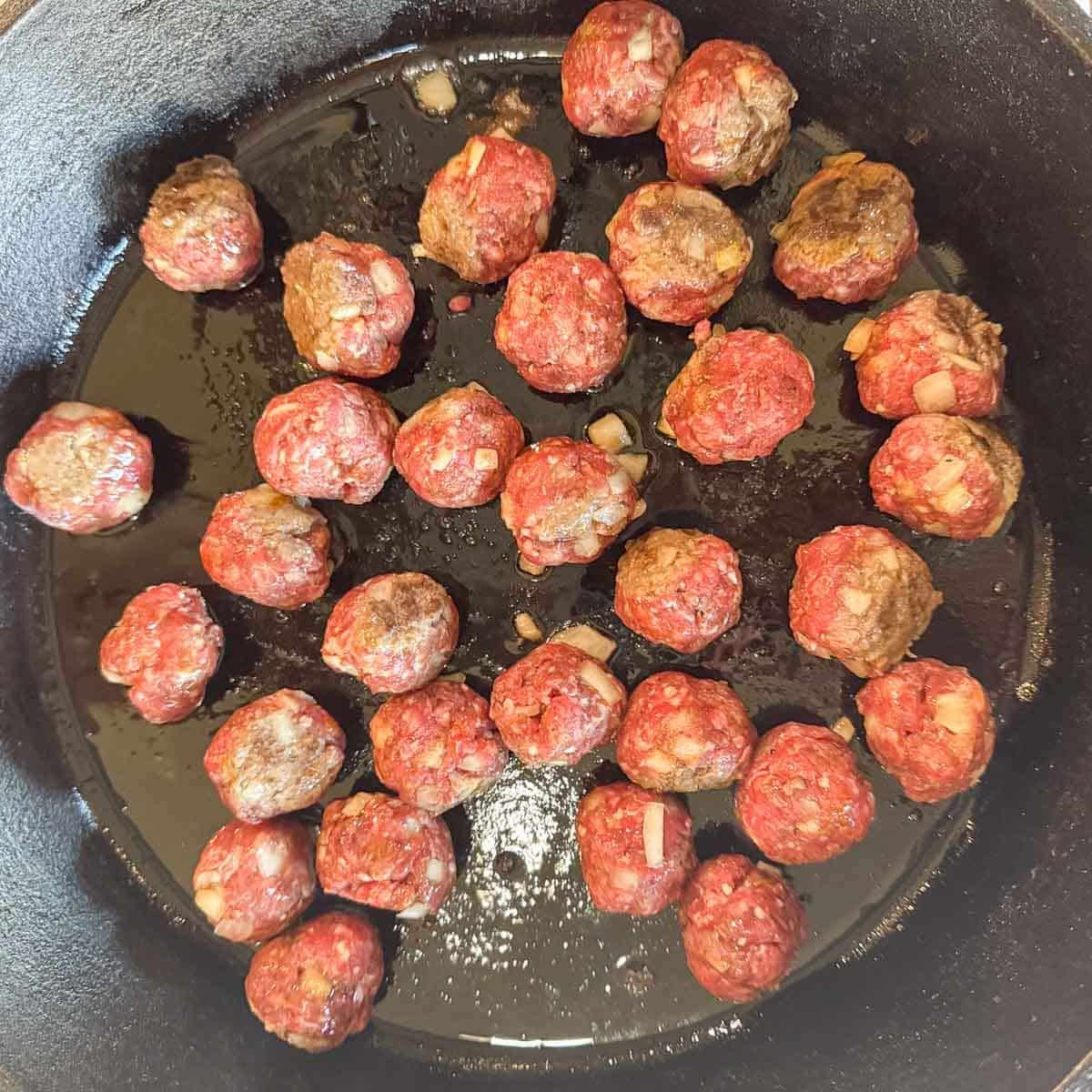 raw meatballs being fried in a pan.