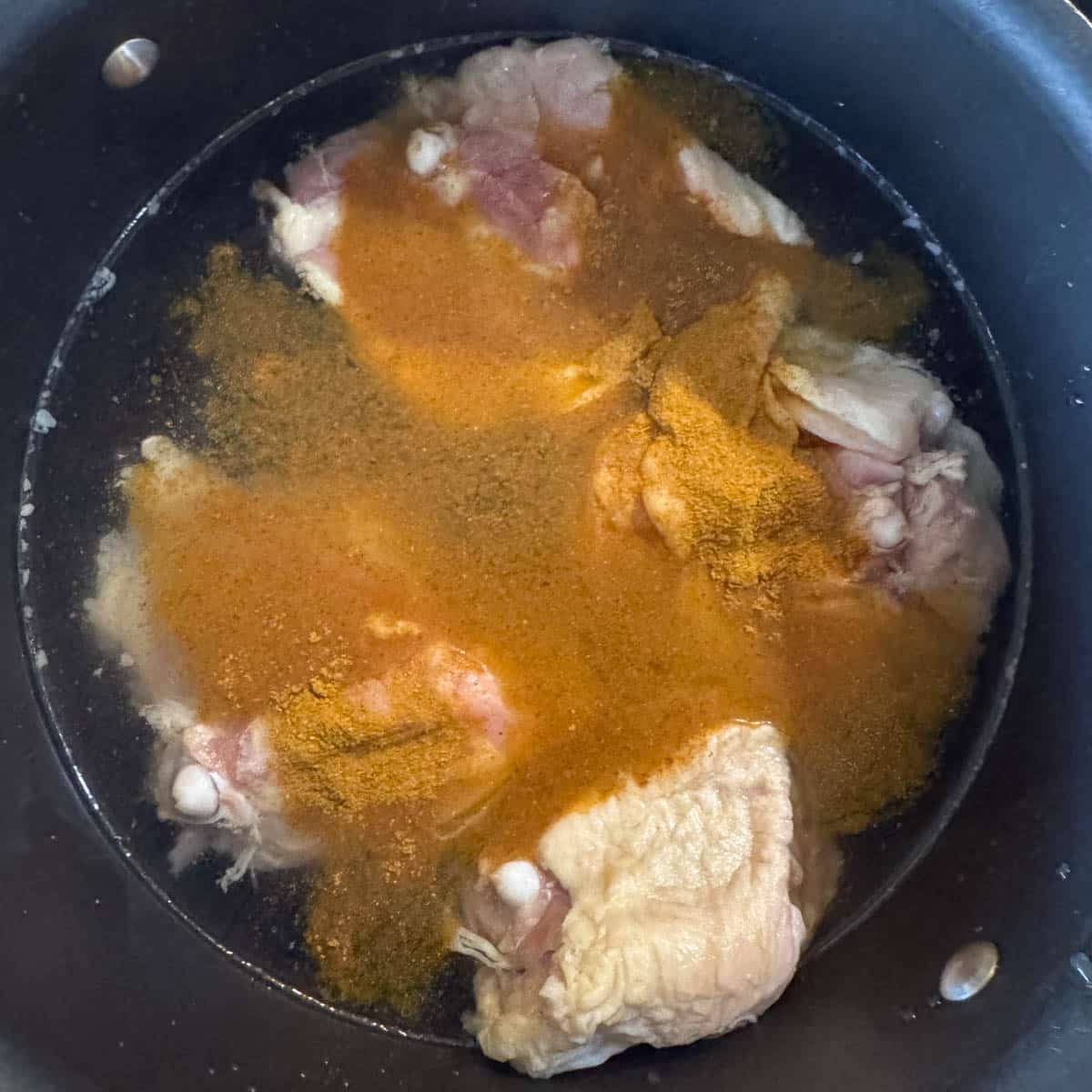 chicken in a pot covered with water and spices.