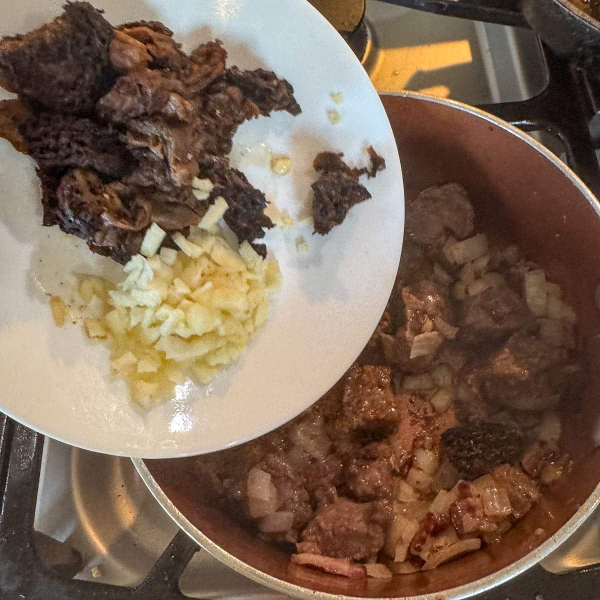 adding mushrooms and garlic to a pot of meat. 