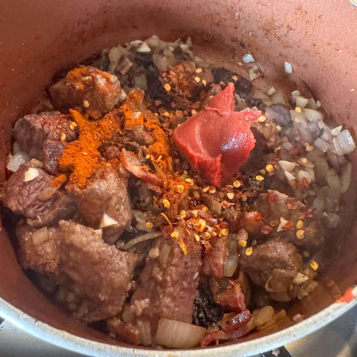 cubed meat, topped with seasoning and tomato paste in a small pot. 