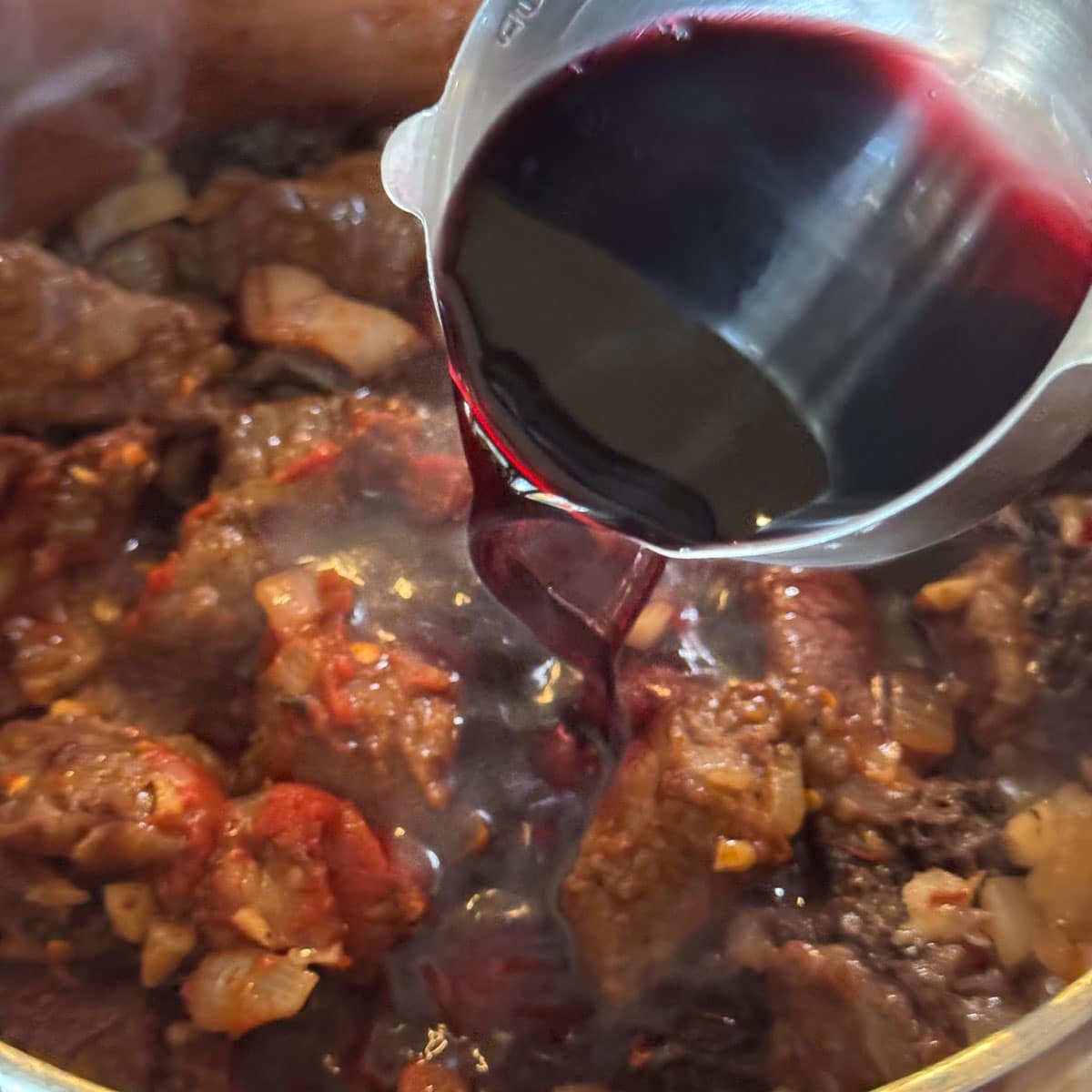 pouring wine over a pot of cubed meat. 