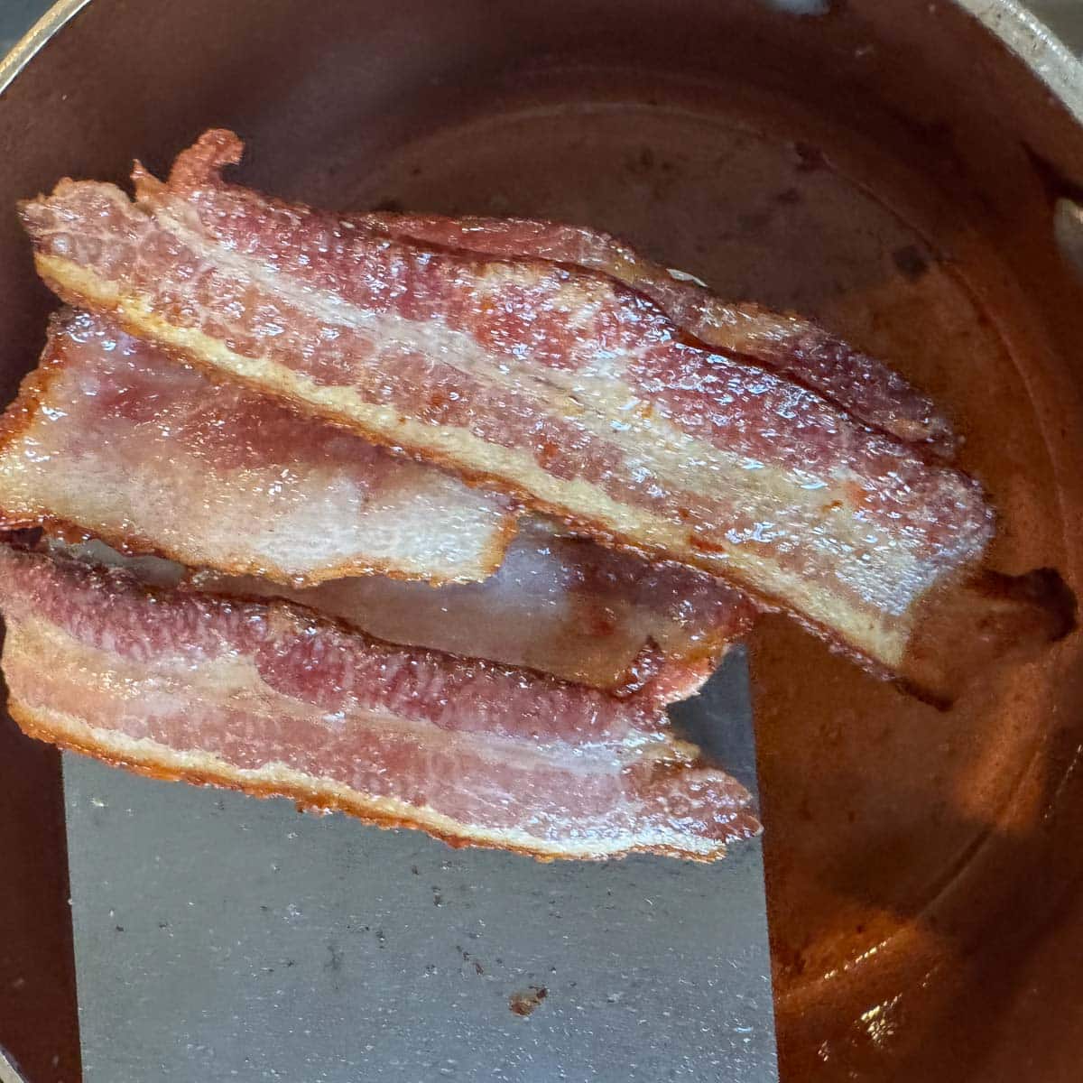 bacon being removed from a pot. 