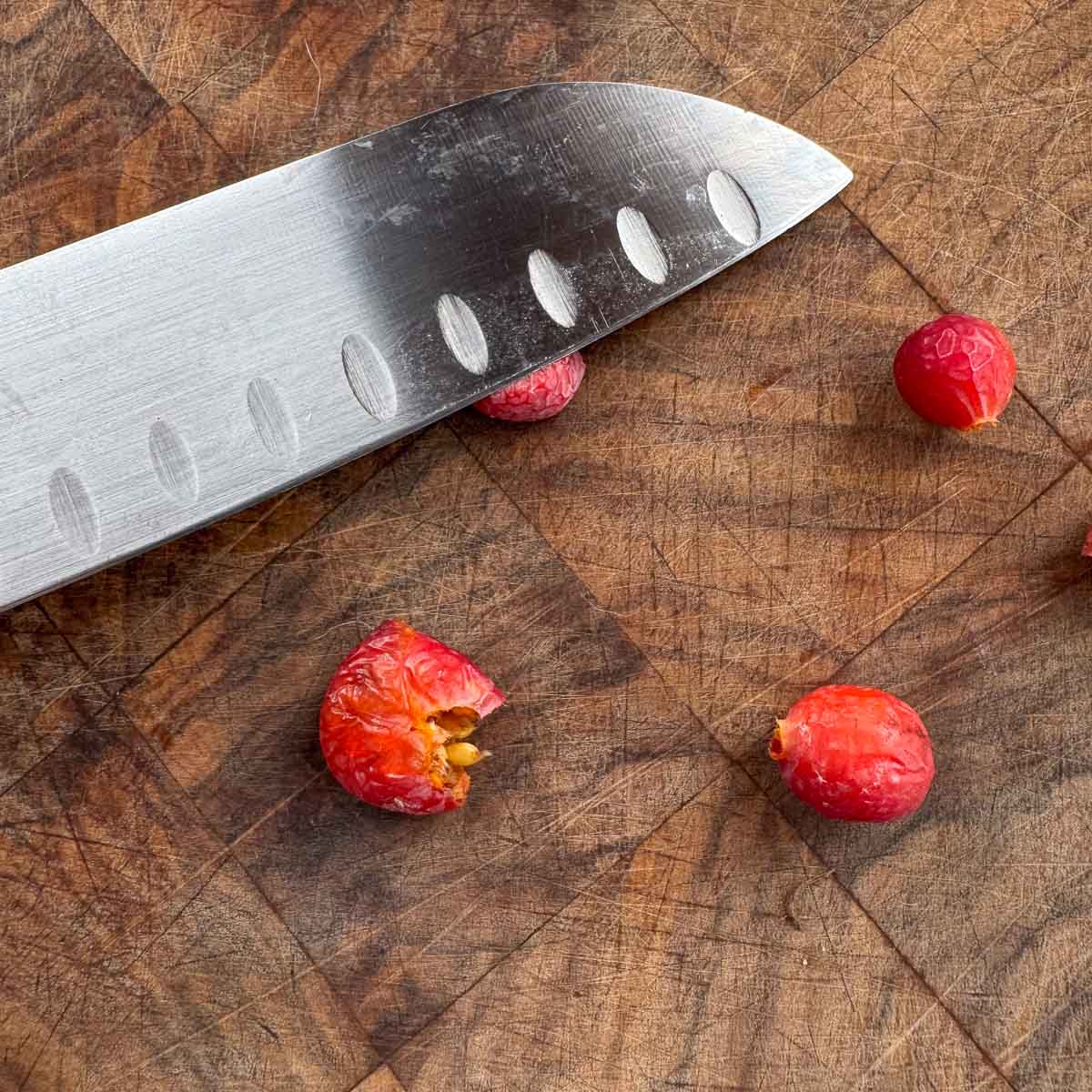 rosehips on a cutting board being smashed with a knife. 