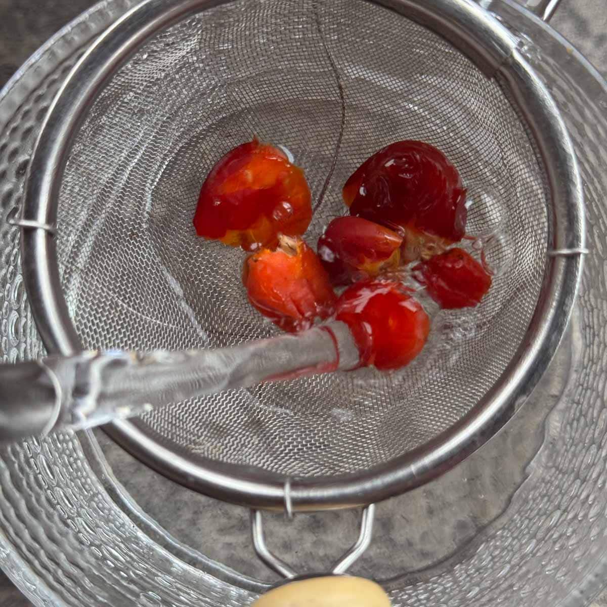 pouring hot water over rosehips in a strainer over a cup. 