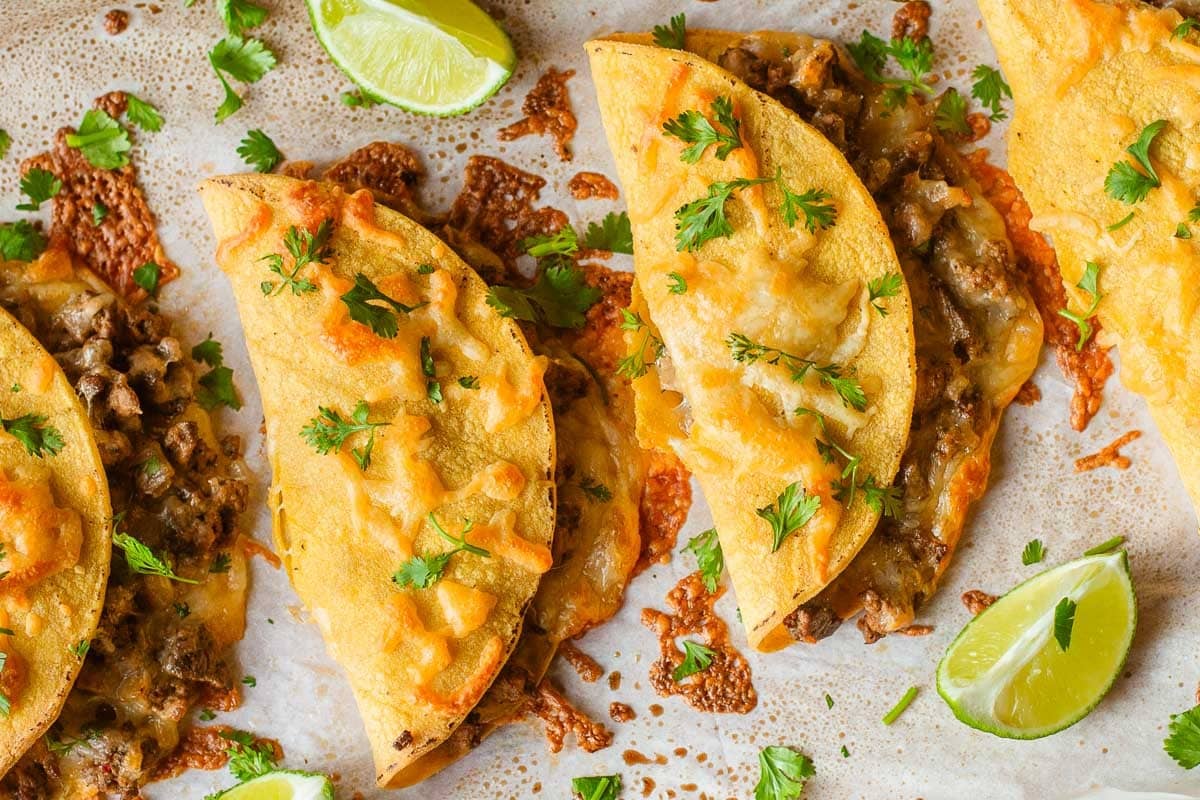 sheet pan tacos topped with cilantro beside lime wedges.