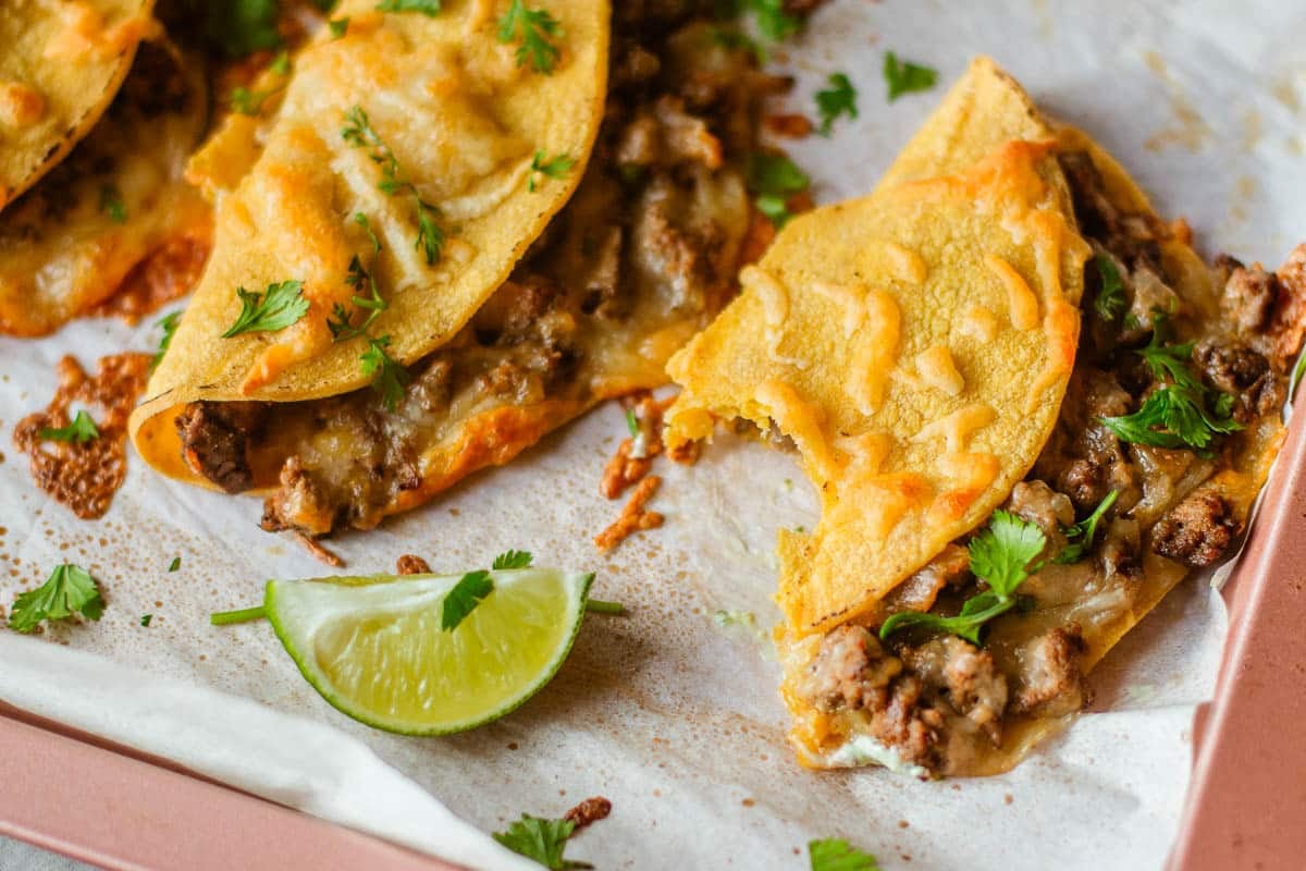 sheet pan tacos with a bite taken out of one beside lime wedge.
