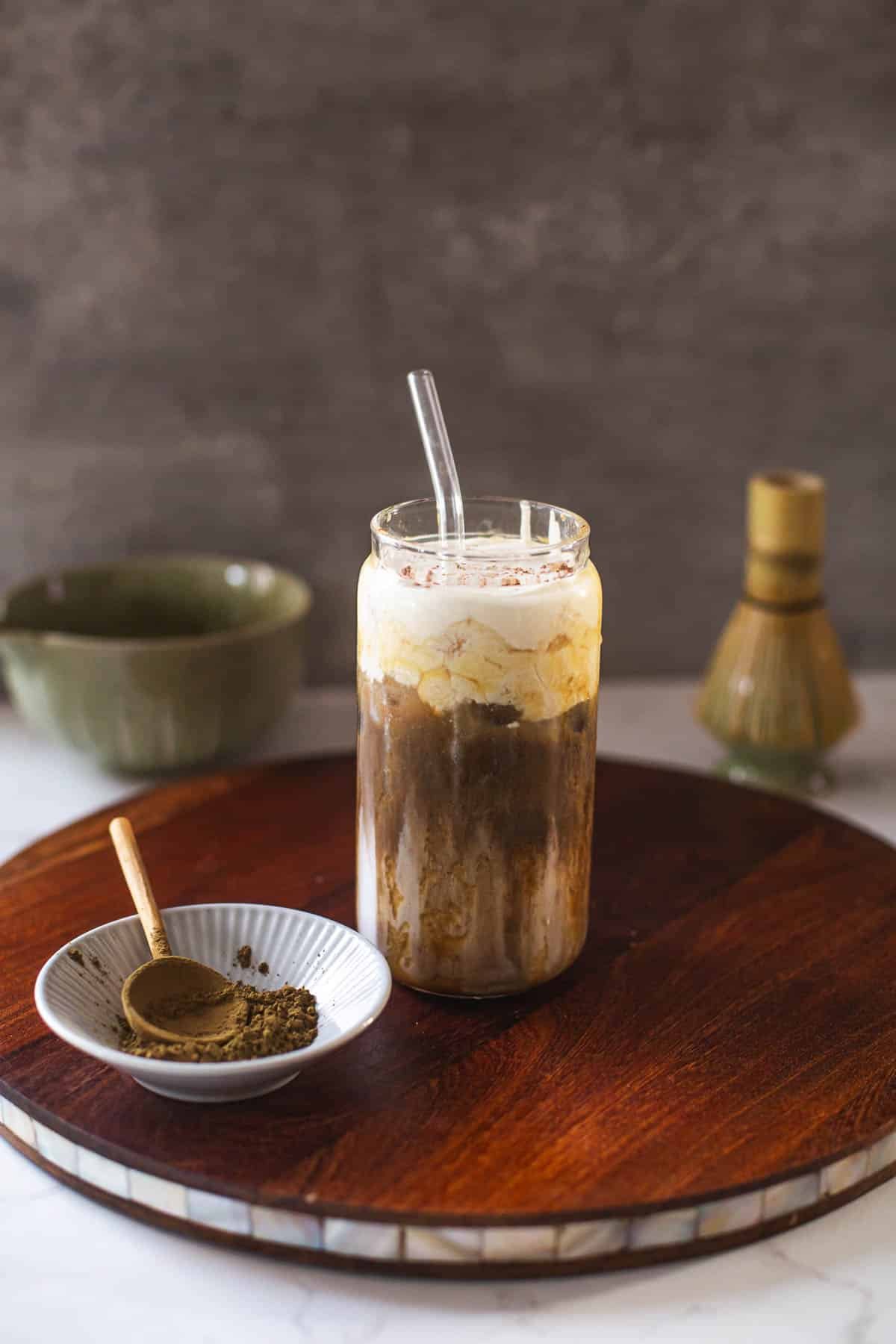 hojicha latte on wooden board with hojicha powder, whisk, bowl of tea.