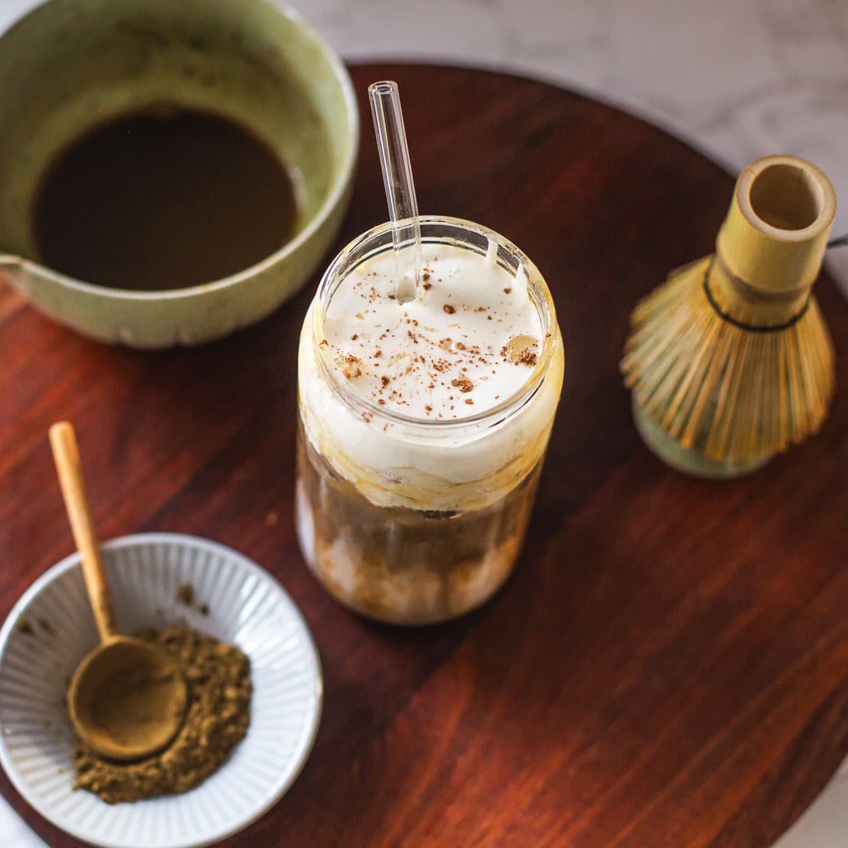 hojicha latte on wooden board with hojicha powder, whisk, bowl of tea.