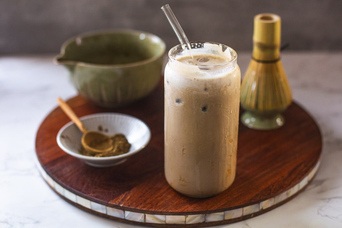 hojicha latte on wooden board with hojicha powder, whisk, bowl of tea.