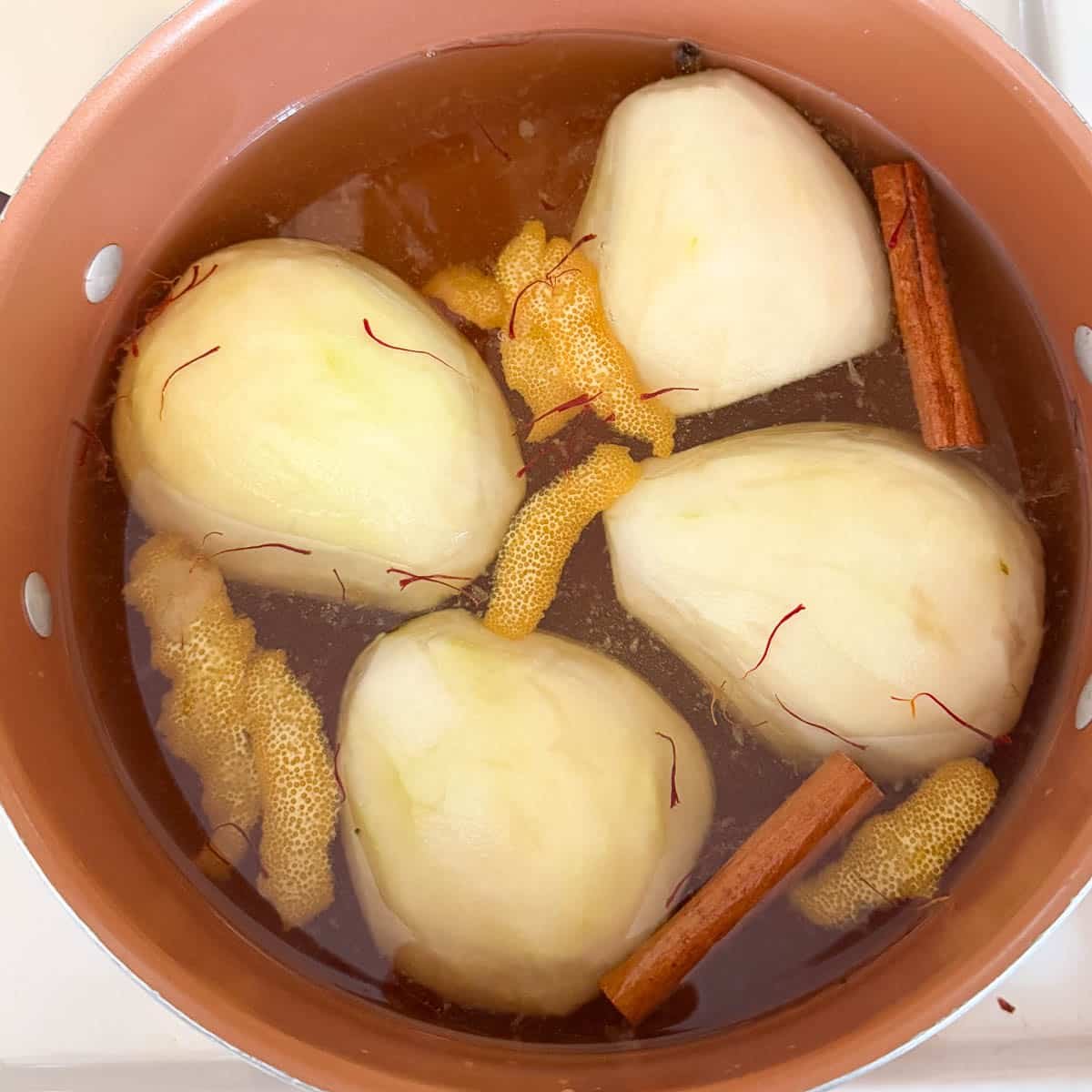 peeled pears floating in poaching liquid with aromatics.