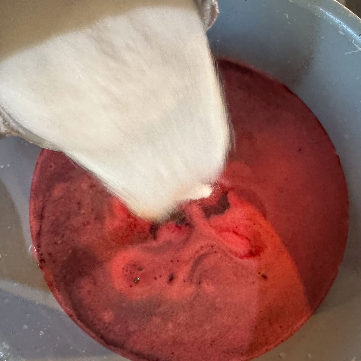 pouring sugar into a pot of pomegranate juice.