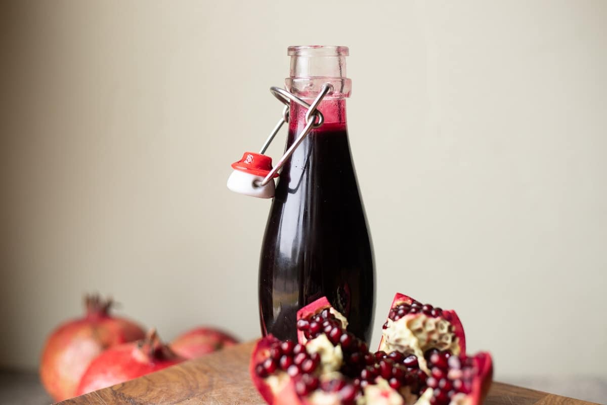 pomegranate syrup in a flip-top bottle with pomegranates around it.