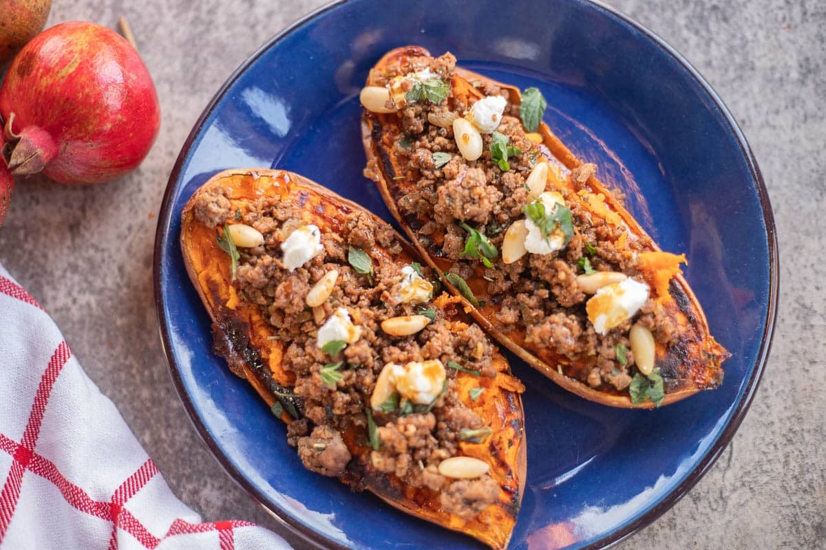 stuffed sweet potatoes on a blue plate with pomeagranates in the background.