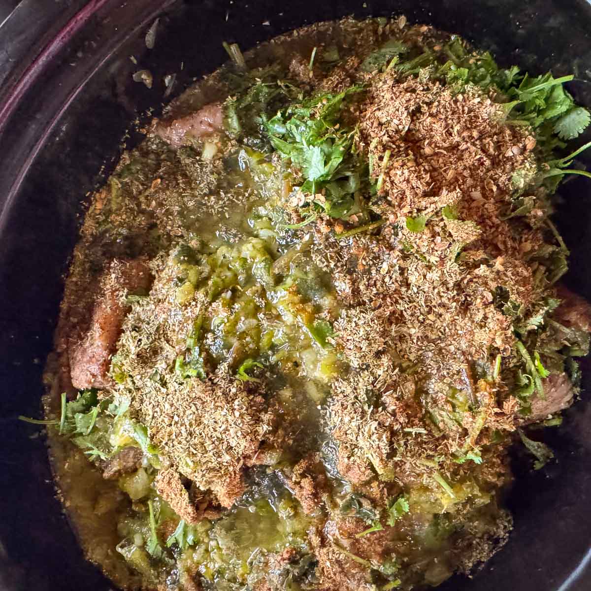 chili verde ingredients in a slow cooker topped with spices