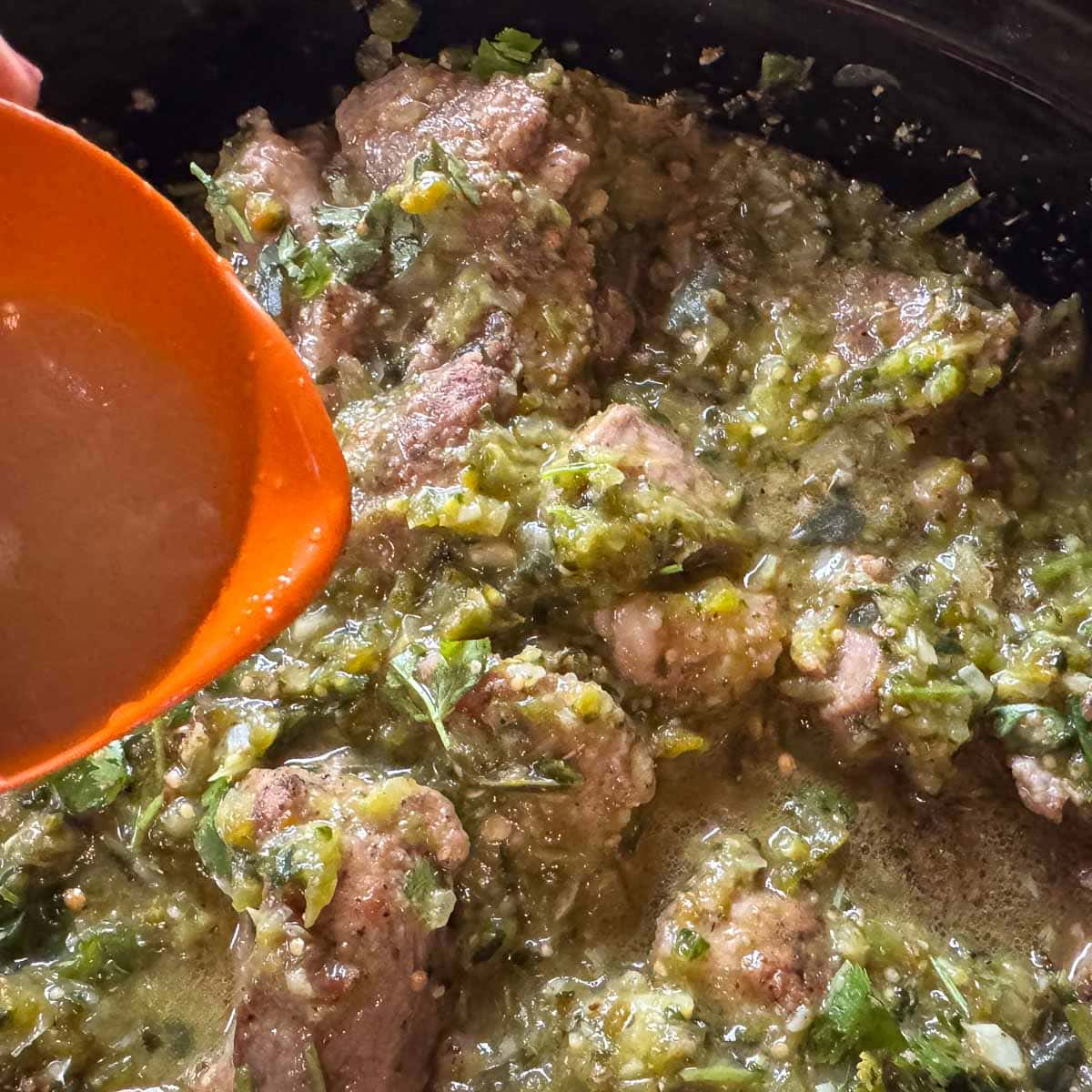 pouring lime juice over chili verde ingredients in a crock pot
