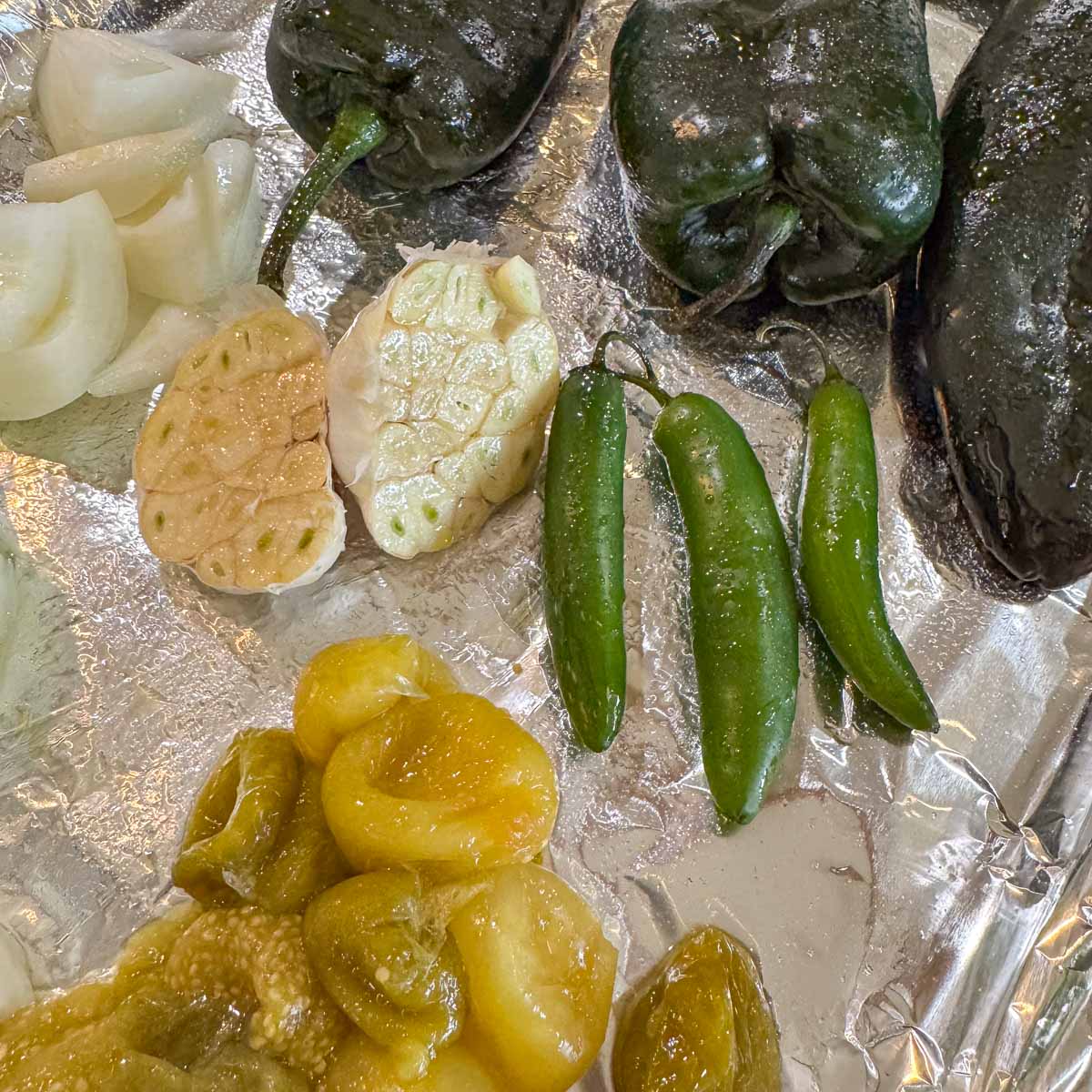 chiles, garlic, onion, tomatillos on a baking sheet.
