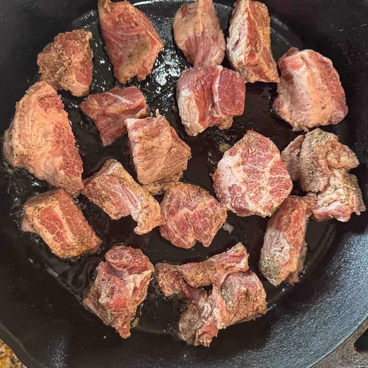 raw cubed pork in a pan before being seared.