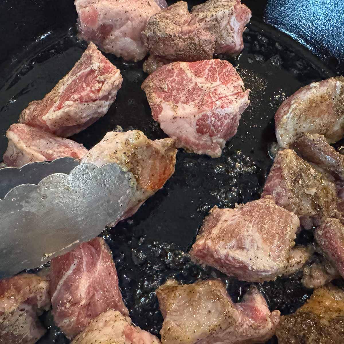 searing cubed pork in a pan for slow cooked pork chile verde.