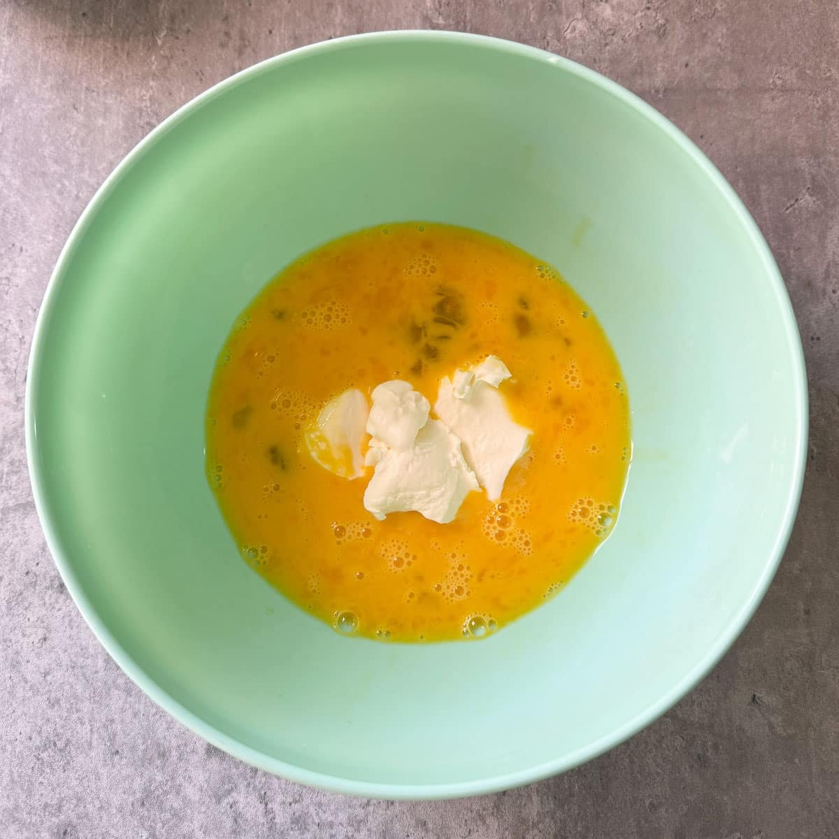 creme fraiche added to egg mixture in green bowl