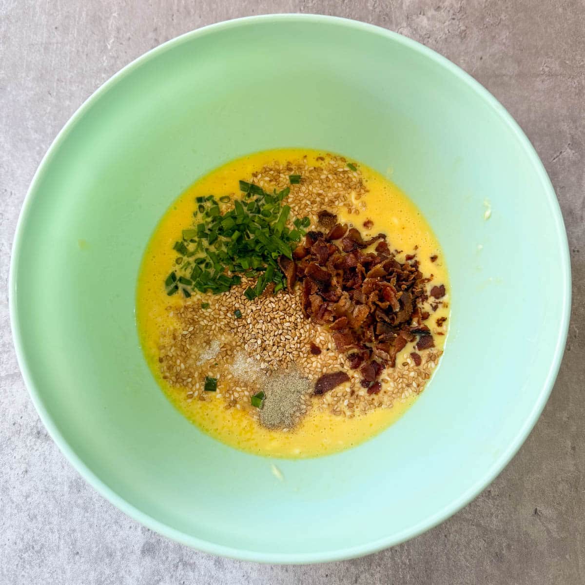 bacon and seasonings added to egg mixture in a green bowl