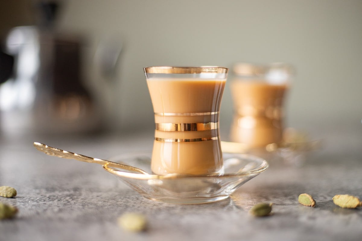 karak tea in little glass tea cups with cardamom pods around it
