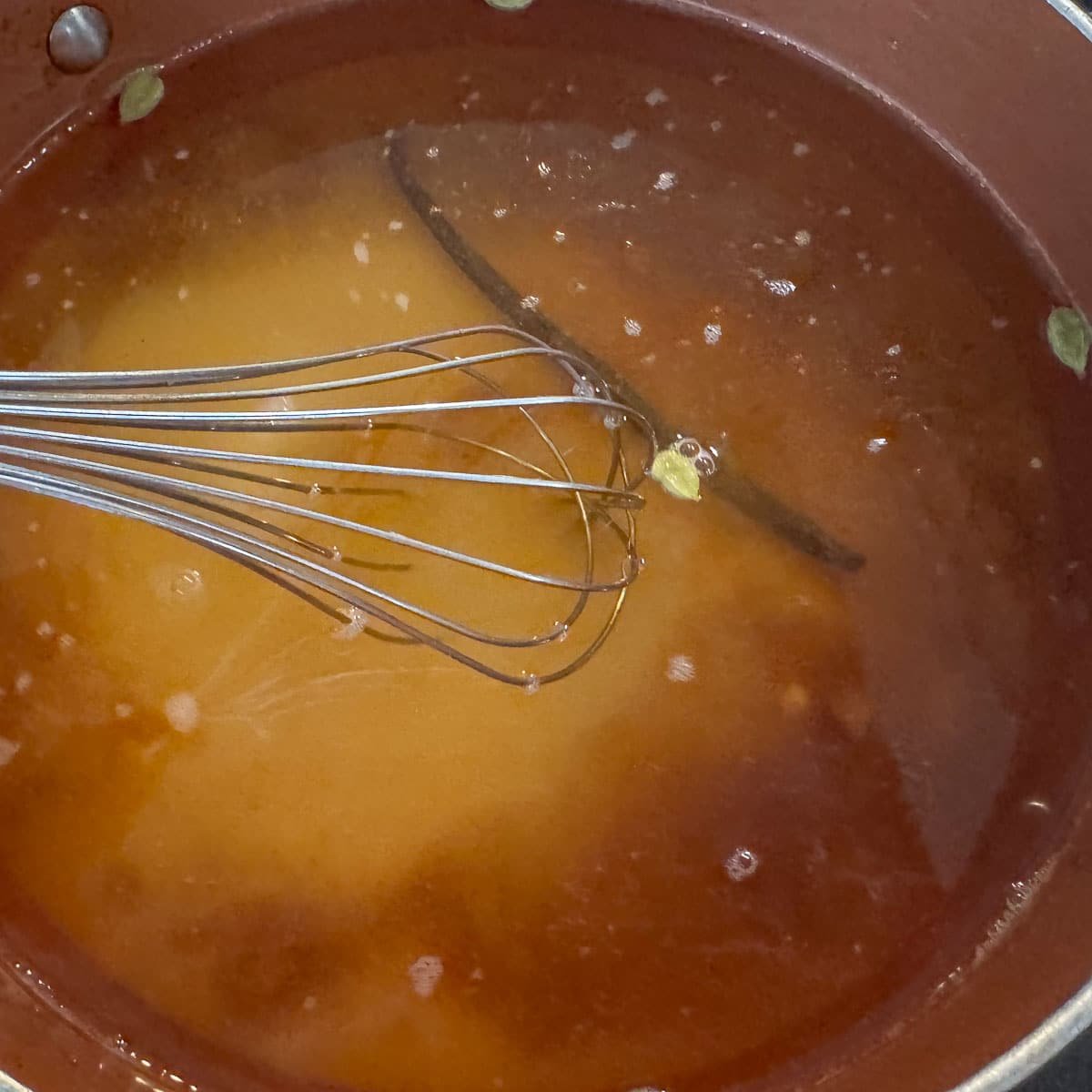 syrup with vanilla bean and cardamom pods being whisked in pan