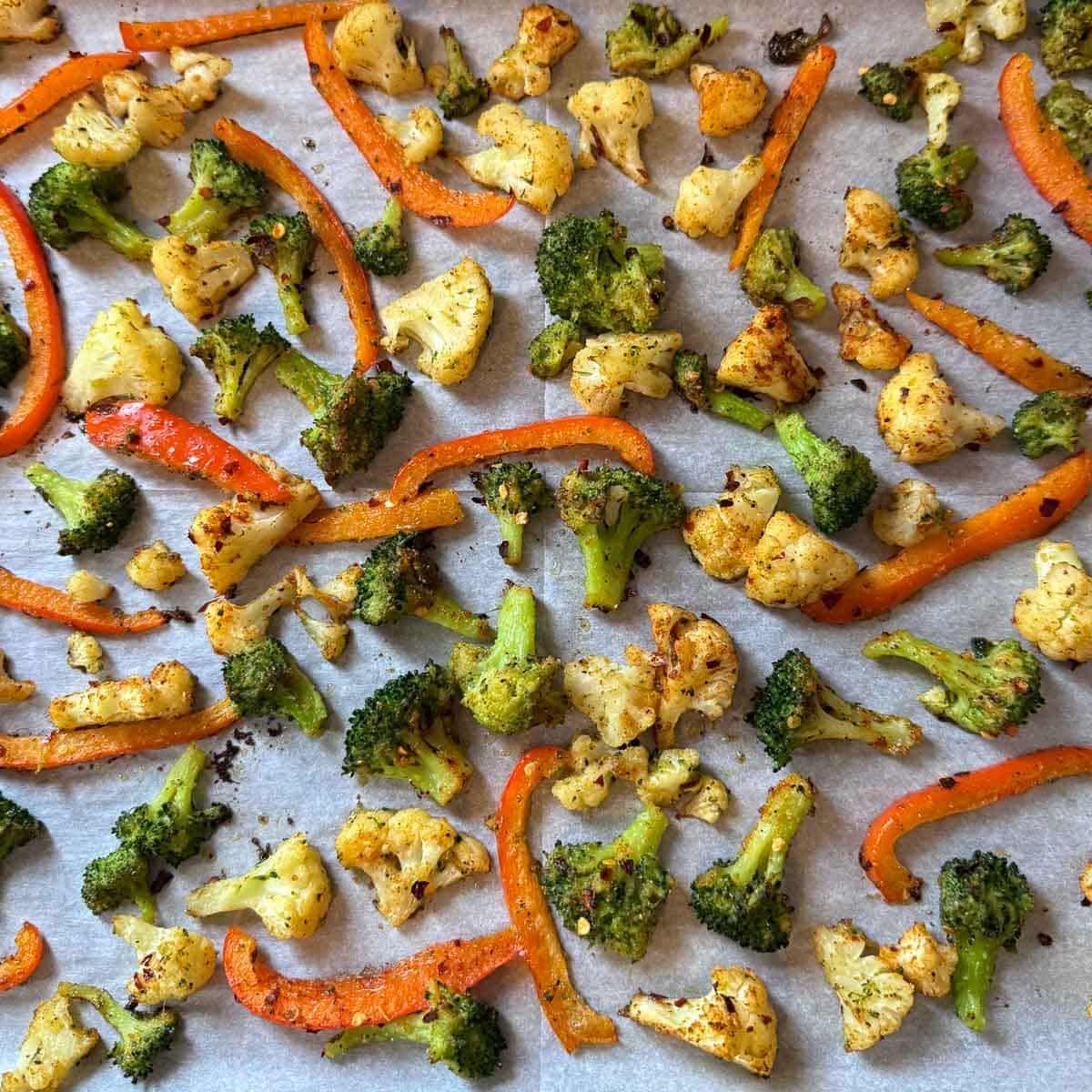 broccoli, cauliflower, and red peppers on baking sheet after first round of roasting.