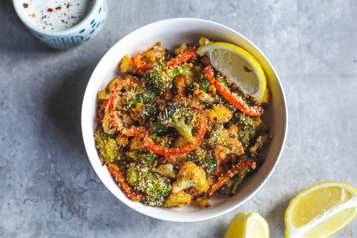 roasted broccoli and cauliflower in bowl beside lemon wedges and bowl of ranch.